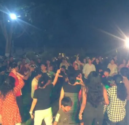 The crowd dances under the night sky at the outdoor sports event party.