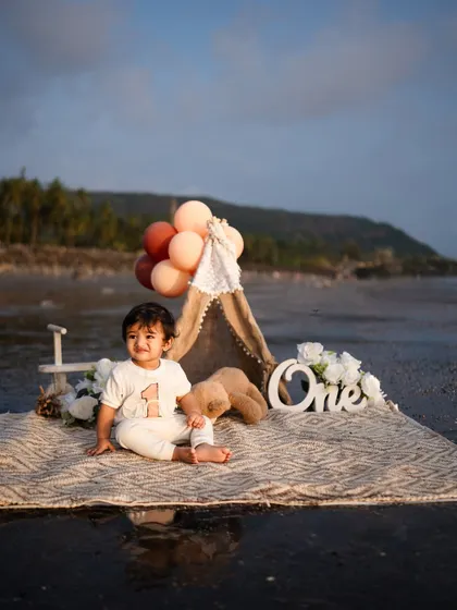 A happy, seated portrait of the baby boy celebrating his first birthday. The combination of the 'One' sign, balloons, and his sweet smile makes for a perfect milestone photograph.