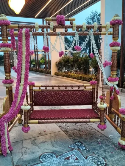 An ornate wooden swing (jhoola) decorated with pink and white floral garlands, serving as a beautiful and traditional seating option for the bride during her Mehendi ceremony.