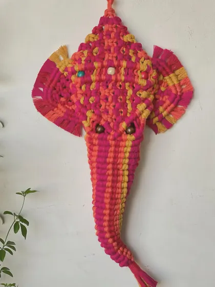 A vibrant, multi-colored macrame Ganesha. I used bright pink and yellow cords to create this beautiful representation of the beloved Hindu deity, perfect for a home altar or as a blessed wall hanging.