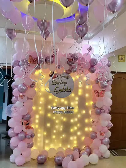 A beautiful home decoration with a pink and lavender balloon arch against a curtain of fairy lights.