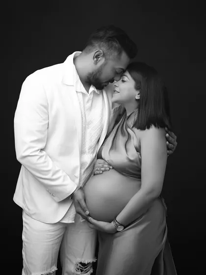 A classic black and white maternity portrait that exudes intimacy and love. The high contrast and simple background keep the focus entirely on the couple's tender embrace.