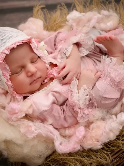 Dressed in an elaborate pink ruffled outfit and bonnet, this newborn sleeps in a rustic nest, looking like a character from a vintage storybook.
