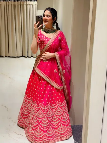 A mirror selfie in a stunning pink bridal lehenga, showing off the intricate gold embroidery. This is a classic look for a bride.