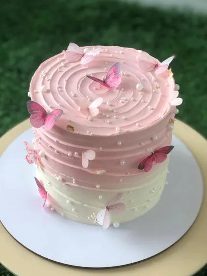 A pink ombre cake with a spiral top, adorned with a flight of pink edible butterflies.