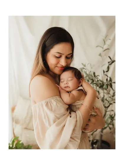 A mother cradling her sleeping newborn in a softly lit, natural setting.