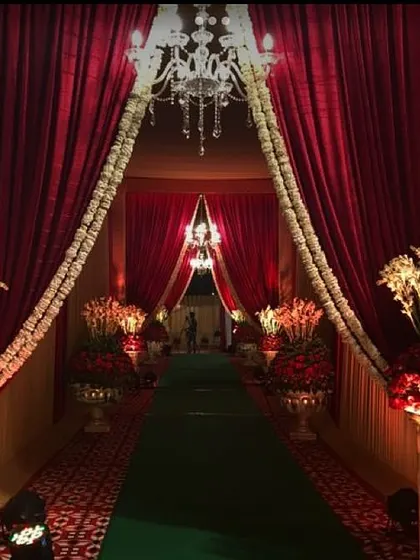 This royal entrance features deep red curtains, large floral arrangements in traditional vases, and a green carpet. The design is perfect for creating a sense of grandeur and heritage.