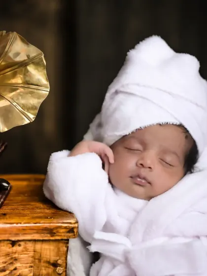 A close-up of a newborn in a spa-themed setup, complete with a tiny bathrobe and a relaxed pose. It's a humorous and adorable take on newborn photography.