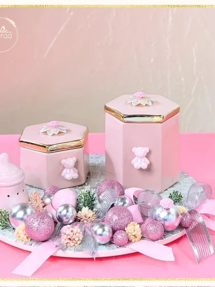 A full view of the sparkling baby girl announcement hamper. The arrangement includes a baby bottle-shaped ceramic, hexagonal jars, and a platter full of festive baubles, creating a truly celebratory feel.