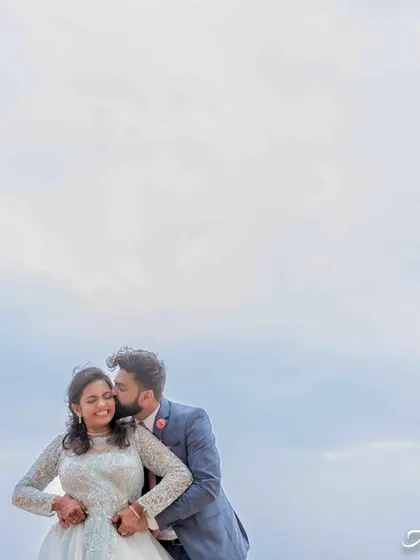 A quiet, romantic portrait against the sky. The use of negative space emphasizes the couple's embrace and the intimacy of the moment.