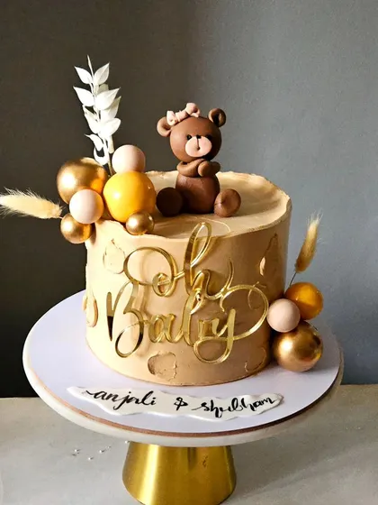 A stylish baby shower cake in a beige monochrome color scheme. This design proves that you don't always need pink or blue, using earthy tones, gold accents, and a cute teddy bear for an elegant look.