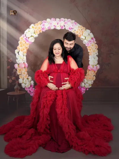 A classic couple's pose. The dad-to-be stands behind his partner, gently holding her as she cradles her baby bump. The floral hoop adds a romantic touch.