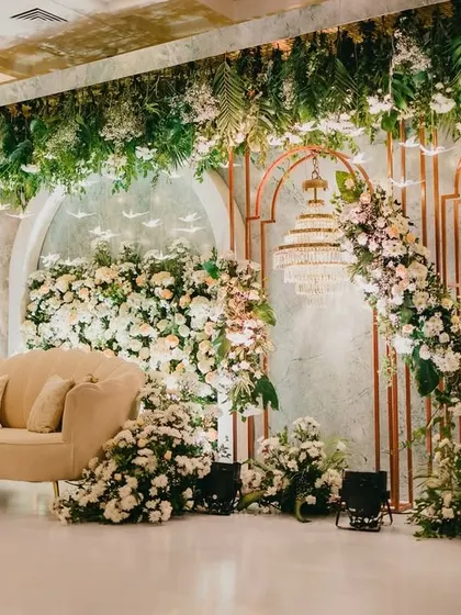 An elegant reception stage with a backdrop of white florals, greenery, and a grand chandelier.