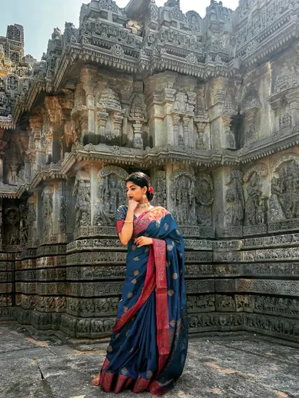 A wide-angle shot capturing the grandeur of a Hoysala temple. I am wearing a blue Kanjivaram saree, and the image showcases both the magnificent architecture and the elegance of the attire.