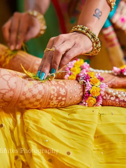 The details matter. This shot focuses on the beautiful floral jewelry being tied to the bride's wrist, highlighting the textures and colors of the Haldi ceremony.