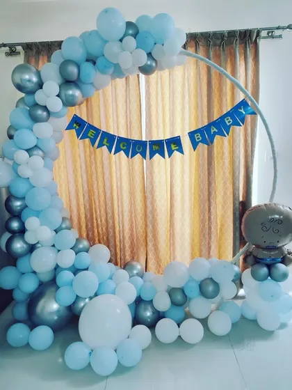 A 'Welcome Baby' setup with a half-moon balloon arch in light blue and silver. A 'Welcome Baby' banner is strung across the center of the ring frame.