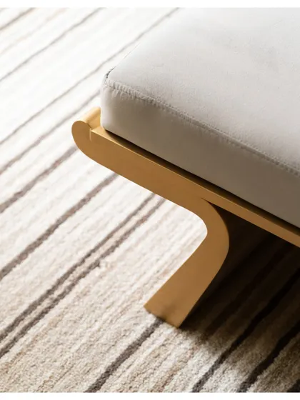 A close-up of the custom-designed bench at the foot of the bed, featuring a unique curved wooden leg that adds a sculptural quality.