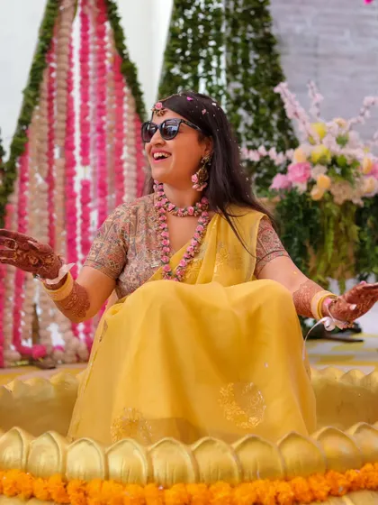 A beautiful, candid shot of the bride laughing in her Haldi seat, wearing sunglasses and enjoying the celebration.