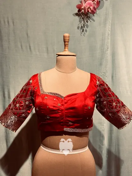 A red silk blouse with delicate linear embroidery on the sleeves, accentuated with bead and sequin detailing.