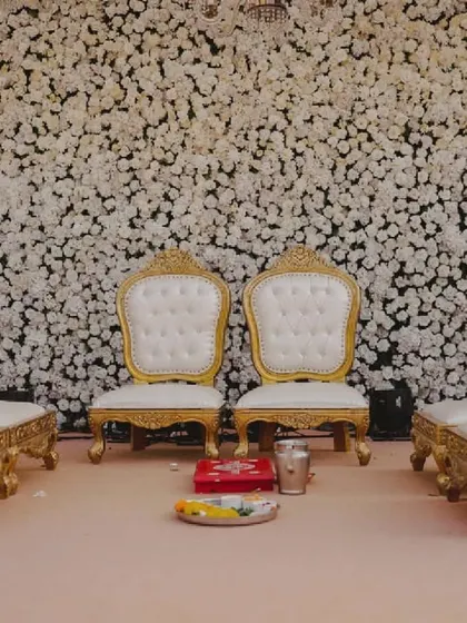 Elegant gold and white throne-like seating for the bride and groom, set against a dense backdrop of white carnations for a truly royal wedding ceremony.