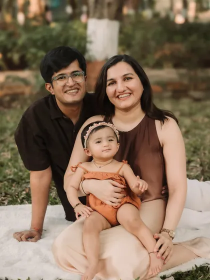 A lovely family portrait sitting on a blanket in the park, smiling warmly for the camera.