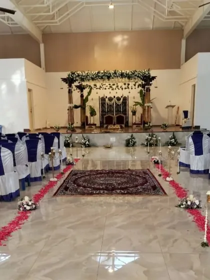 The complete ceremony hall setup, featuring blue and white chair covers that complement the traditional mandap, with a petal-lined aisle creating a formal and welcoming path for guests.