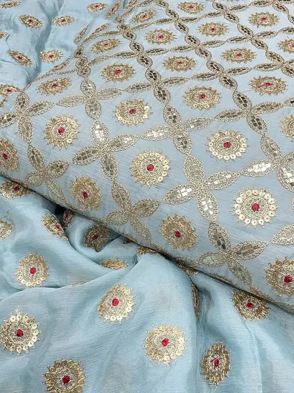 The light blue Chinon fabric, folded to display its body and drape. This material is perfect for boutique owners sourcing high-quality, embroidered textiles for their collections.