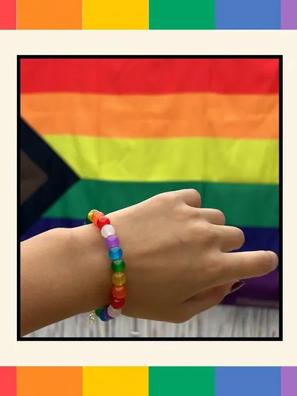 A single hand wearing a rainbow-colored Ally Bracelet, held up in front of the Pride flag. This image captures the personal commitment to allyship that our workshops aim to foster.