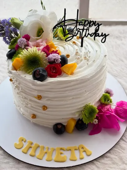 A white cake with a cascade of fresh, colorful flowers and fruits. This design is perfect for summer celebrations, bringing a burst of freshness and color.