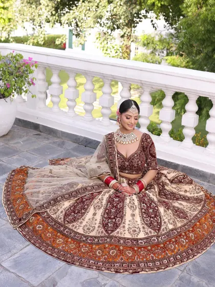 The bride seated, showcasing the beautiful flare and detailed border of the beige and maroon lehenga. The outdoor setting highlights the richness of the colors.