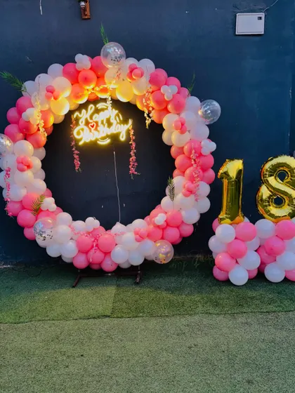 An 18th birthday celebration with a pink and white balloon ring, a neon sign, and large gold foil number balloons.