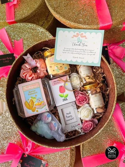 Inside the glam baby shower favor box: a curated selection of treats, a scrunchie, a small frame, and a thank you card from the mom-to-be.