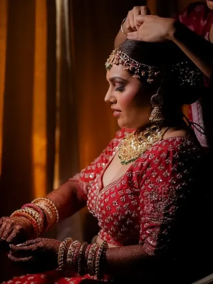A dramatic getting-ready shot of the bride, with a helper adjusting her hair. The chiaroscuro lighting adds a timeless, painterly quality.