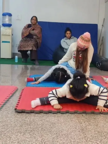 Stretching is fun, especially with friends. Here, our youngest students work on their forward bends and straddle stretches on colorful mats, learning the basics of flexibility in a group setting.