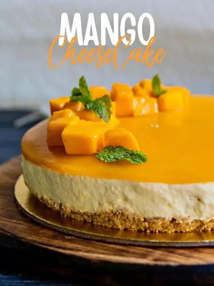 Our Mango Cheesecake, elegantly presented on a marble stand. It features a smooth mango glaze and is topped with fresh mango chunks and mint, making it a refreshing seasonal dessert.