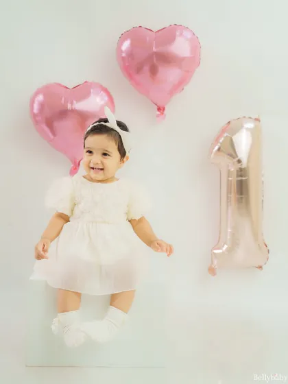 A princess turns one! This sweet portrait with heart-shaped balloons and a simple "1" captures the magic of a first birthday for a baby girl.