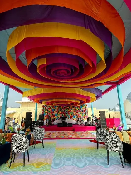 A vibrant carnival-themed event with a swirling, multi-colored fabric ceiling that creates a sense of playful energy. The seating is a mix of colorful and zebra-print furniture, adding to the whimsical atmosphere.
