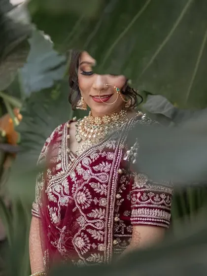 A shy bride peeks out from behind lush green leaves. This creative portrait is playful and artistic.