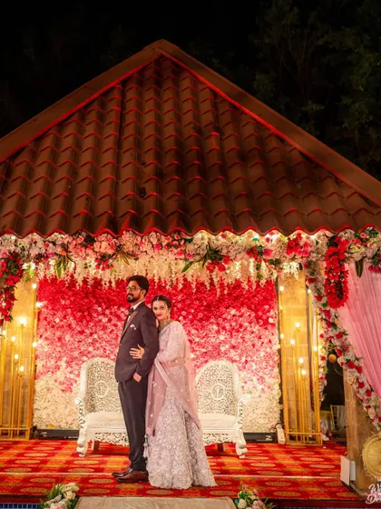 A portrait of the couple on their reception stage. The red and white floral backdrop creates a rich and festive setting for their first photo as a married couple.