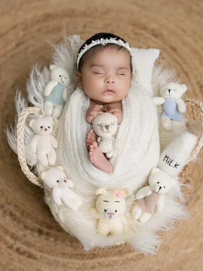 An overhead shot of a newborn nestled in a heart-shaped basket, surrounded by tiny teddy bears. The natural jute background provides a lovely, earthy texture.