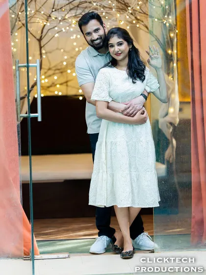 A happy and welcoming pose, with a couple embracing and waving from a doorway decorated with fairy lights.