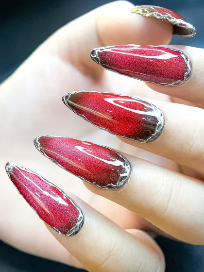 Another view of the red cat-eye nails, showcasing the long, elegant almond shape and the liquid-metal look of the silver border.