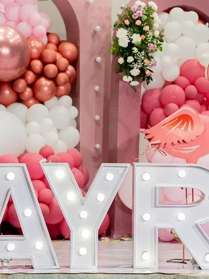Large, illuminated marquee letters spelling "AYRA" add a personalized touch to this pretty-in-pink first birthday party.