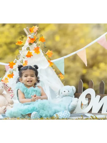 A happy smile from the birthday girl. Nitya is surrounded by her favorite teddy bears in this shot from her first birthday celebration, dressed in a lovely blue party dress.