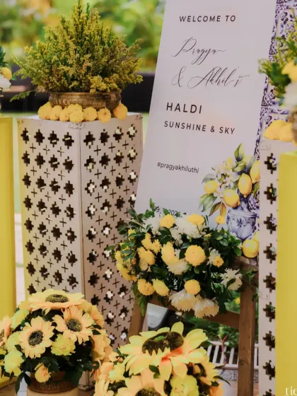 A welcome sign for a "Sunshine & Sky" themed Haldi, surrounded by beautiful arrangements of sunflowers and other yellow blooms.