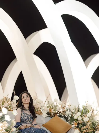 A portrait of the bride at her Roce ceremony. She is seated comfortably amidst the elegant white floral arrangements in front of the modern arched backdrop.