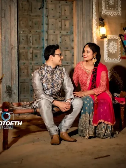 A pre-wedding shoot with a traditional, rustic village theme. The couple is dressed in ethnic wear, sitting on a charpai, creating an authentic and charming scene.