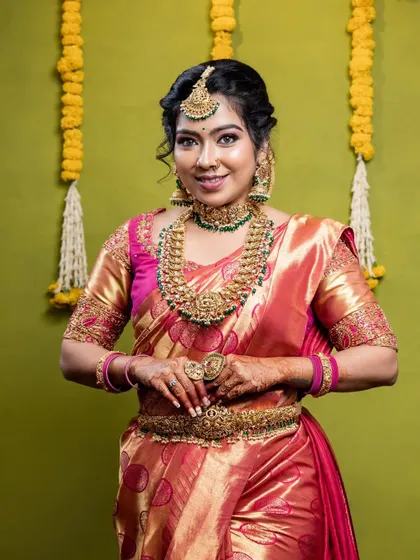 This bride looks absolutely radiant in a classic temple jewellery set with green stone accents. The choker and haram combination is a timeless choice for a muhurtham.