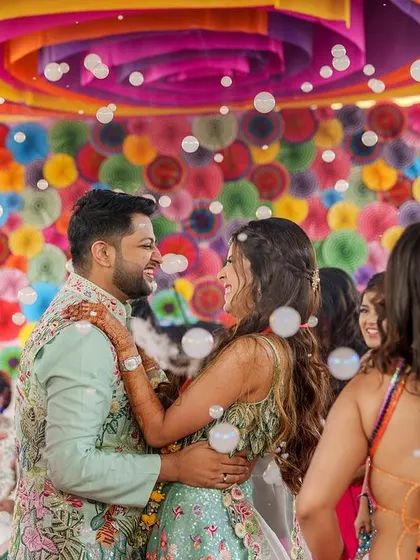 The happy couple enjoying the Carnival party, surrounded by friends and a shower of bubbles. The colorful backdrop of paper fans adds to the joyful, carefree moment.