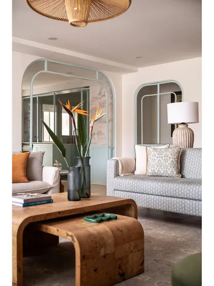 The living room overlooks the dining space, framed by an open metal partition in a soft French blue. This design element defines the areas while maintaining an open, airy feel.